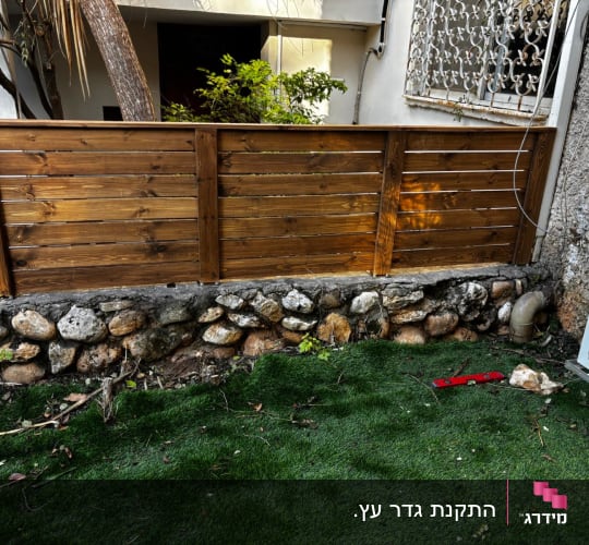 גדר עץ עם אבנים ודשא סינתטי
